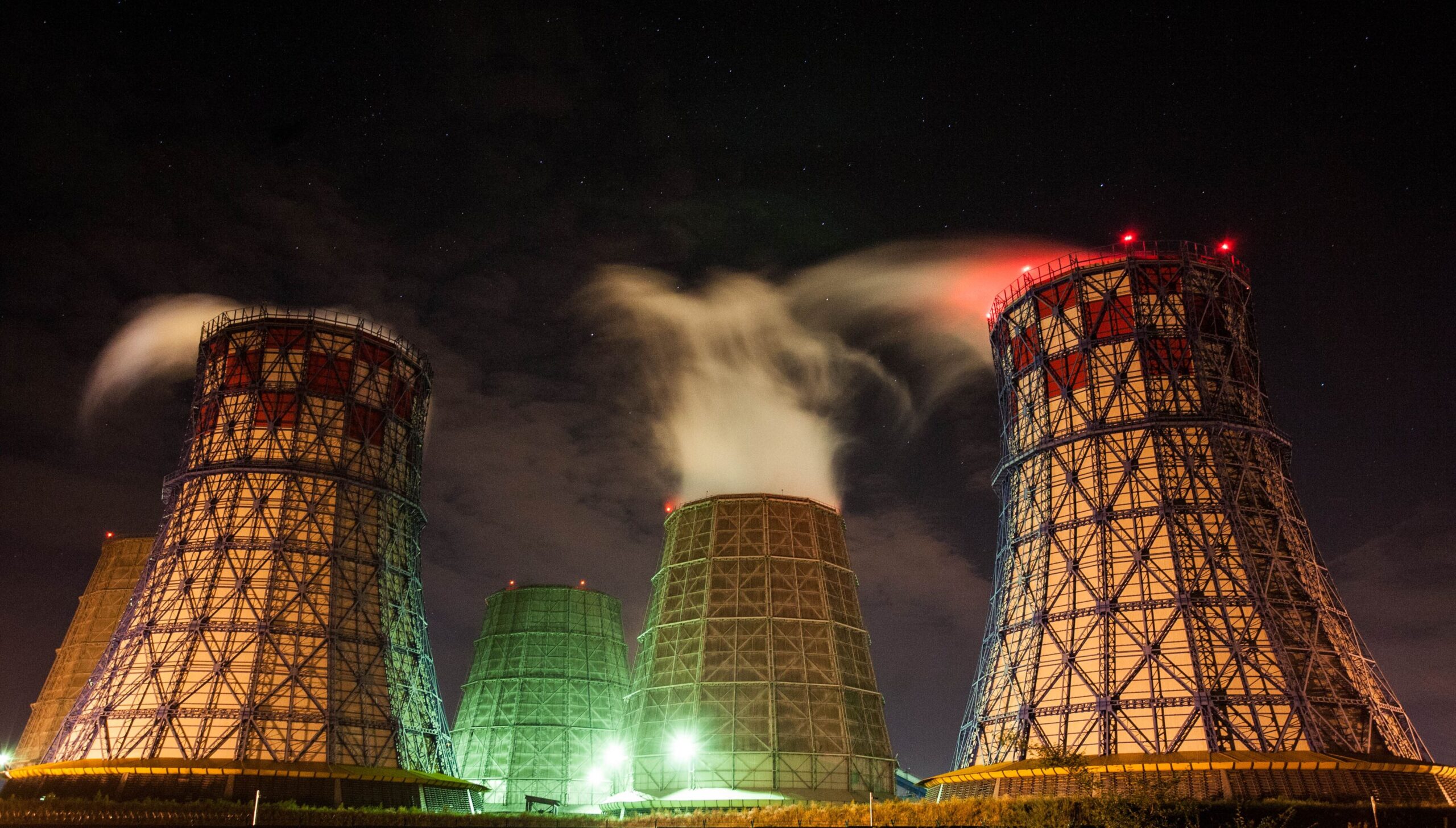 Cooling towers illuminated at night, emitting steam into the dark sky, showcasing industrial energy production.