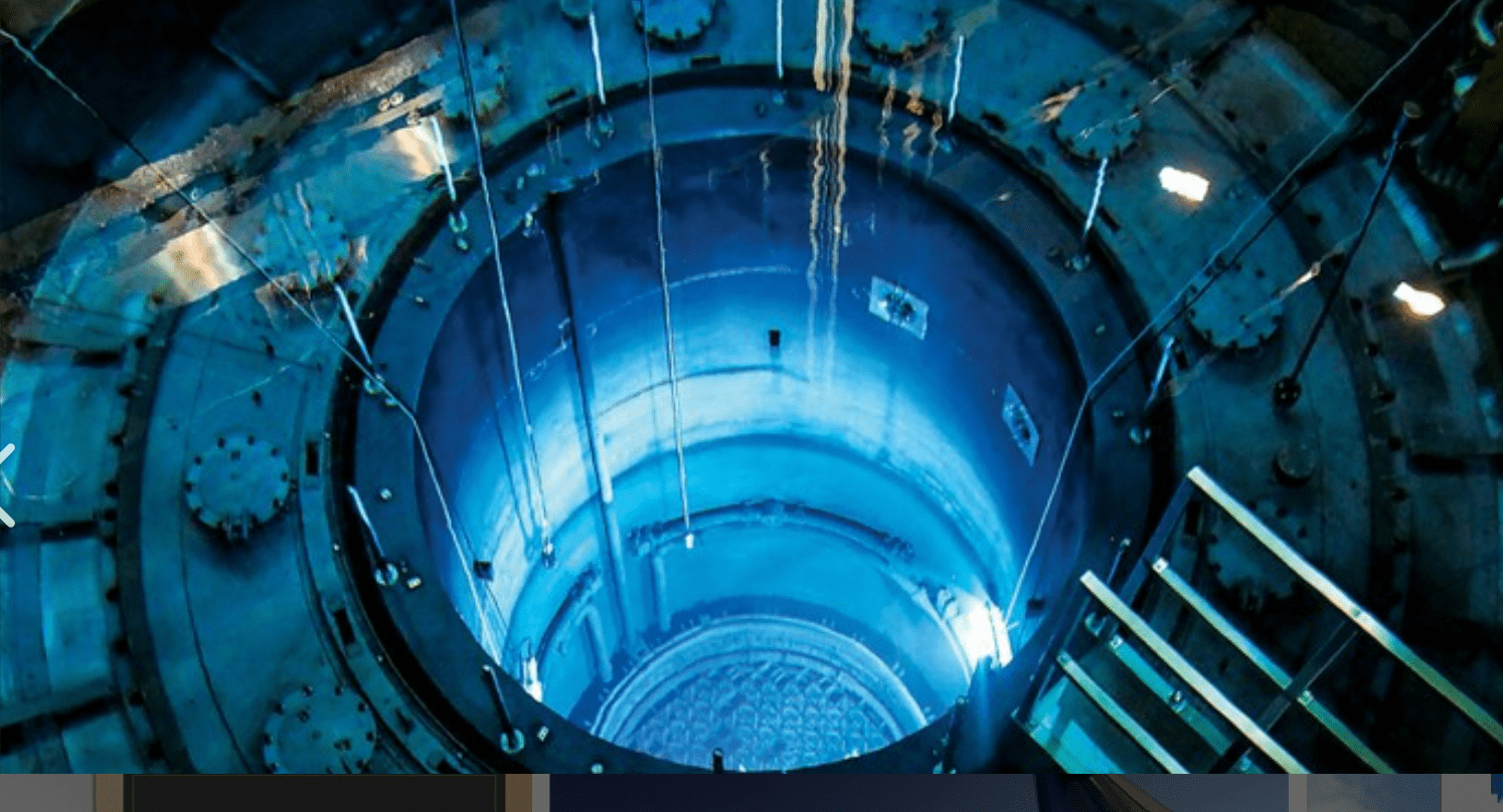 A high-angle view of a cylindrical structure illuminated in blue, revealing the interior of a nuclear reactor. The image conveys the engineering and design of the facility.